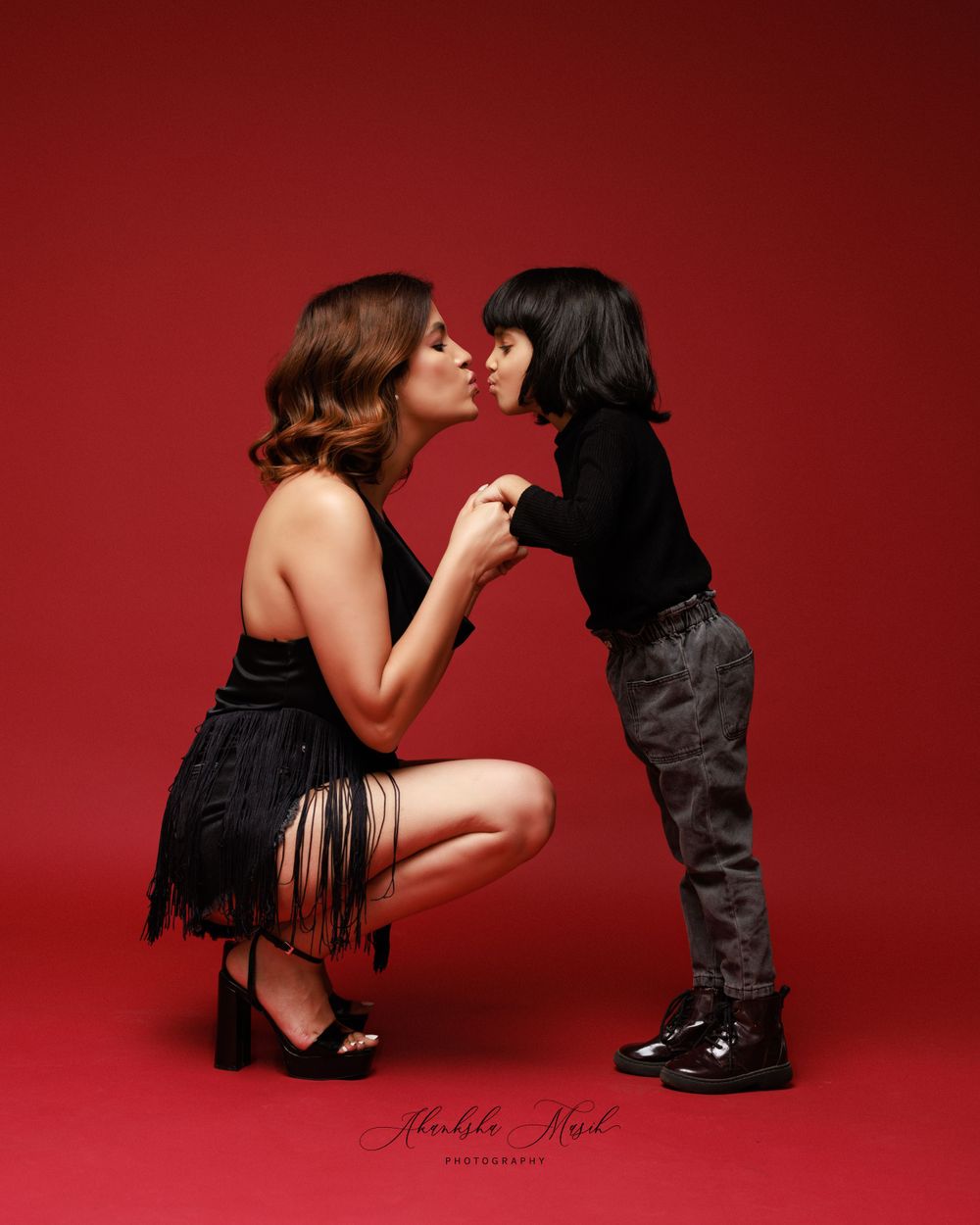 Sweet moment captured against red backdrop in vintage-style portrait.