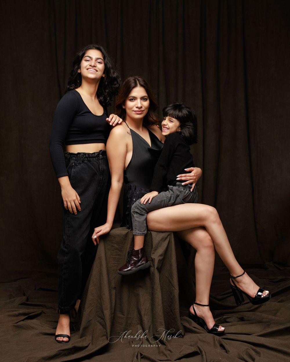 Studio portrait of three people in black outfits against dark background.
