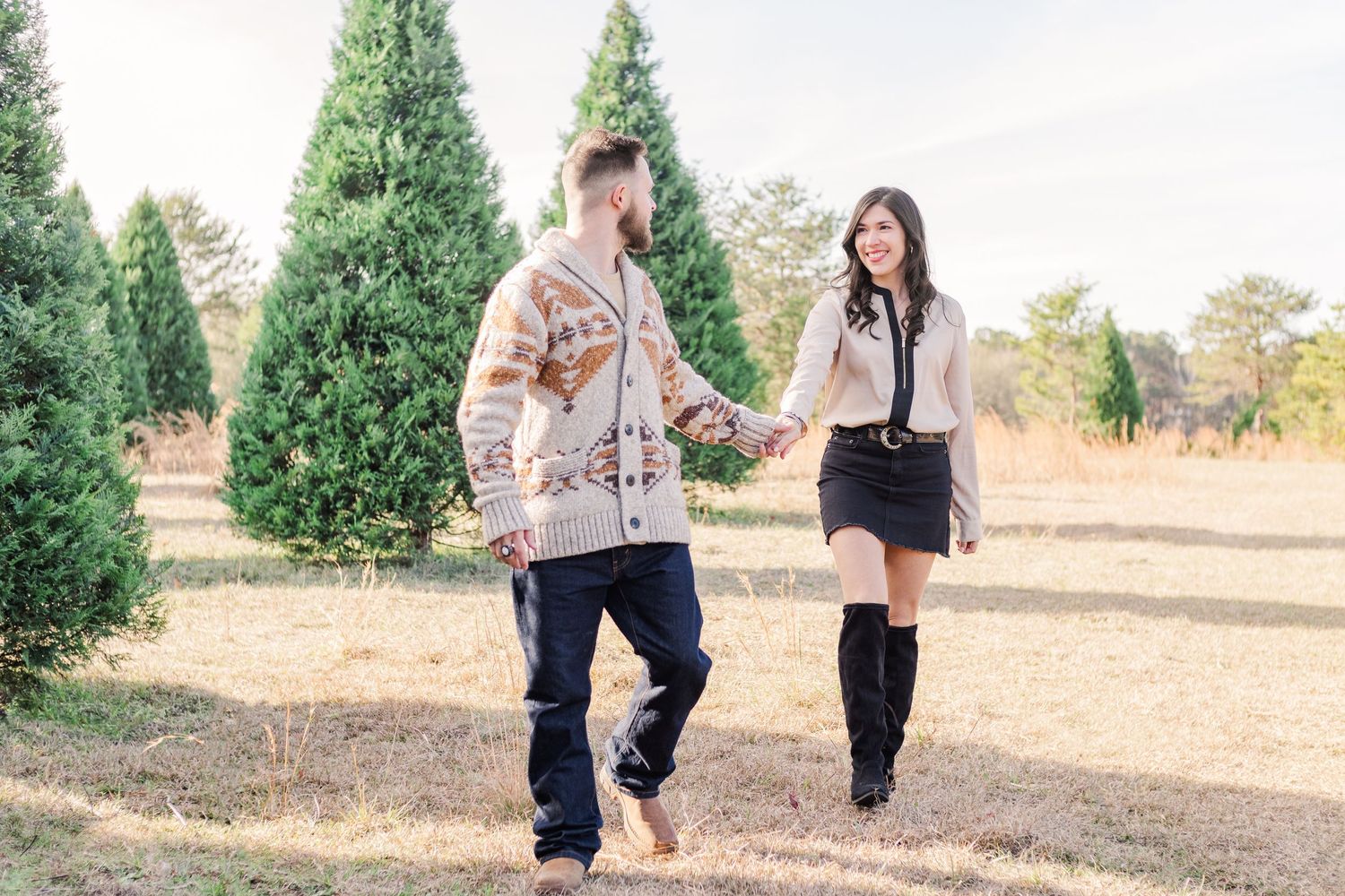 Couple walking hand in hand through scenic tree farm during autumn photo session.