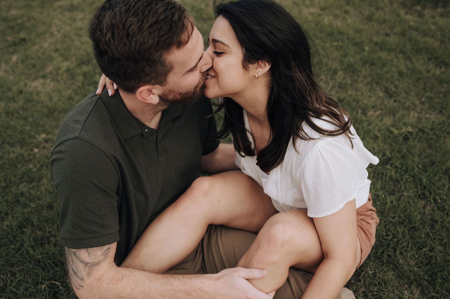 A couple shares an intimate moment sitting together on grass during sunset.