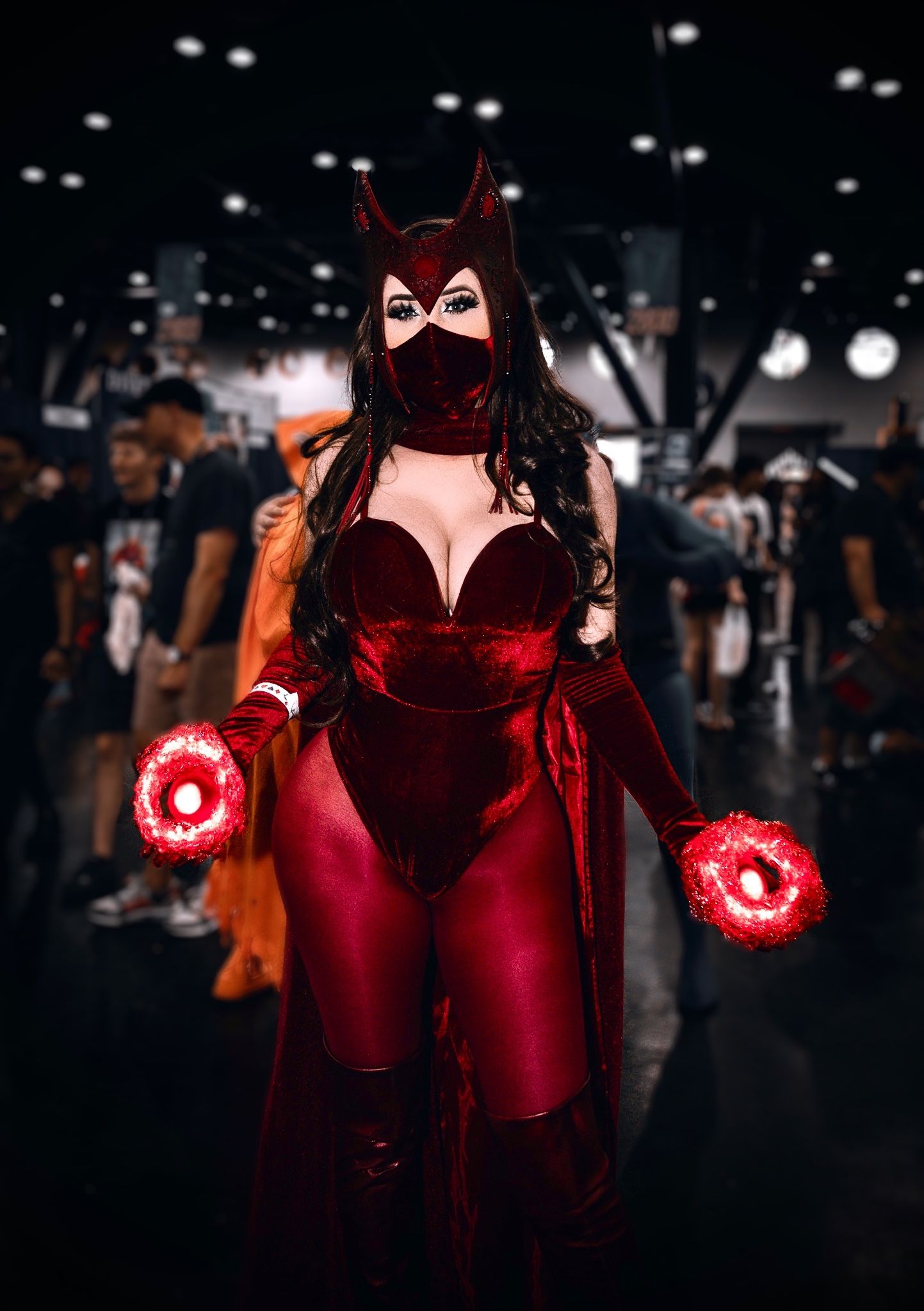 Cosplayer in red velvet costume with glowing magical effects in dark setting.