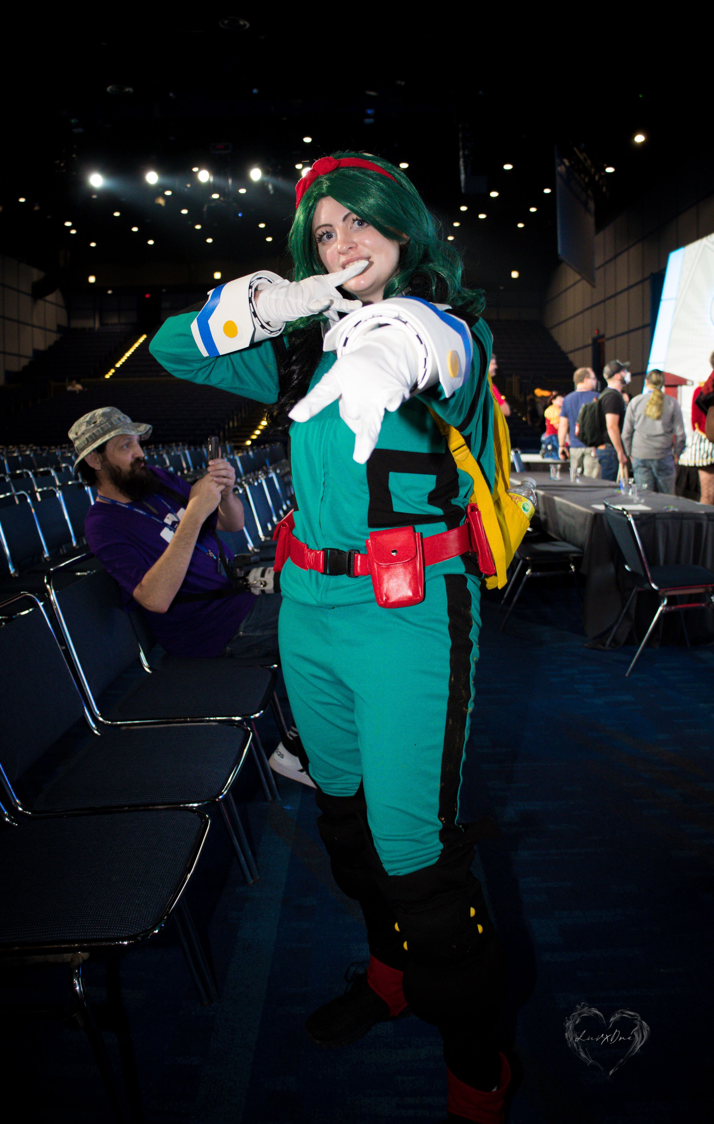 Cosplayer in green military-style uniform poses dramatically at convention.