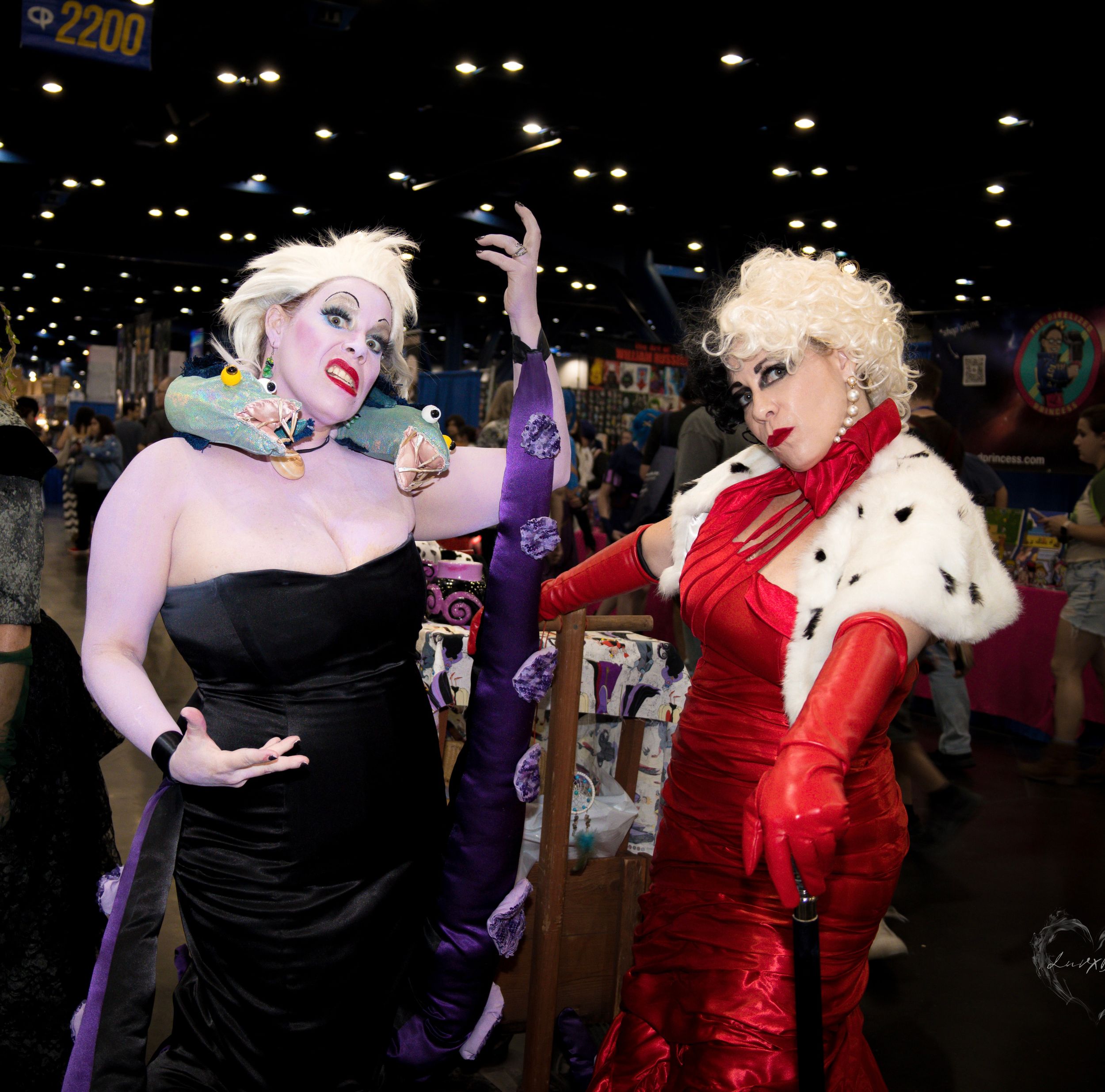Two cosplayers in glamorous evening wear costumes pose dramatically at a convention.