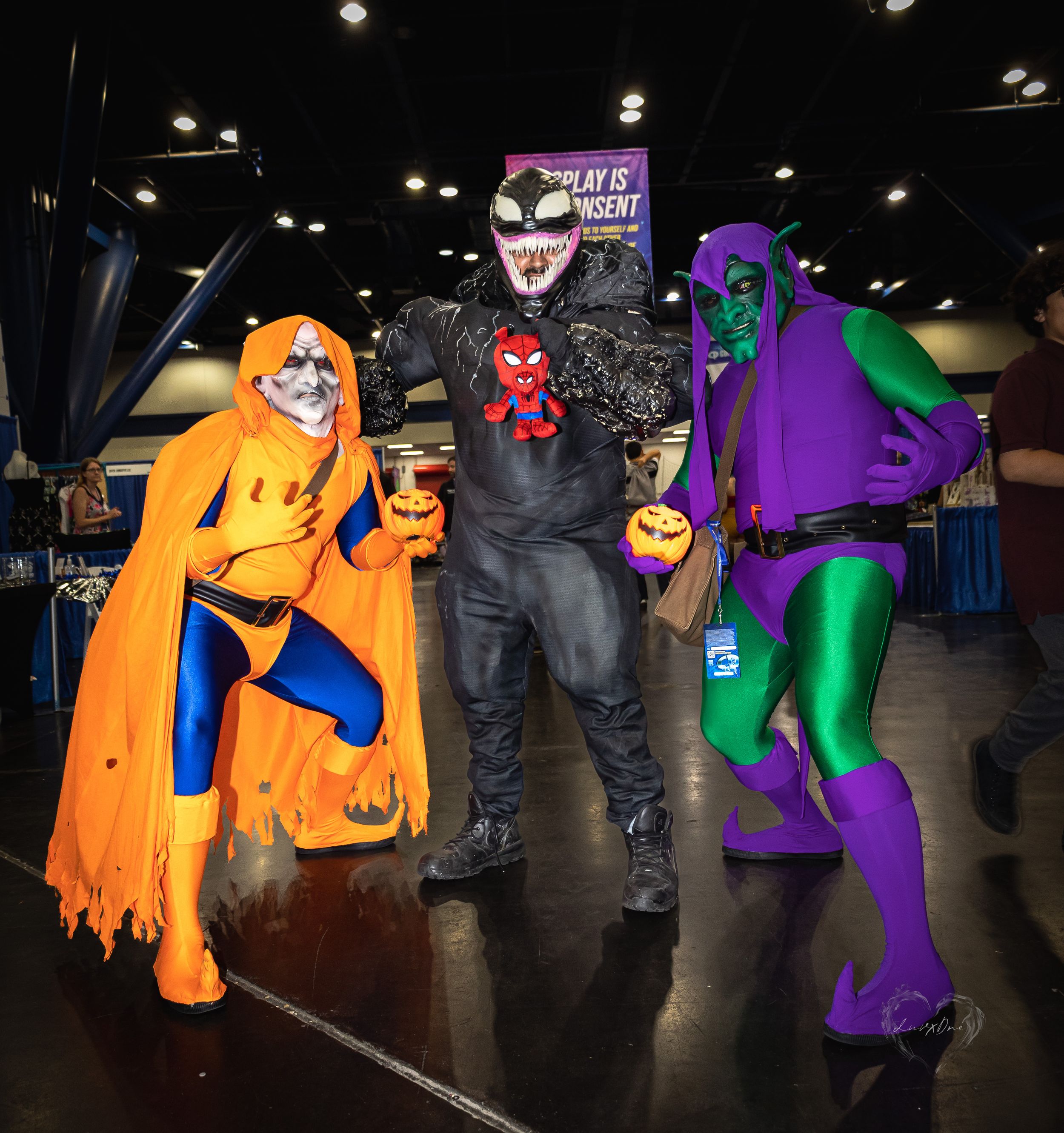 Three costumed characters in orange, black and purple outfits pose together at a comic convention.