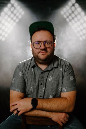 Portrait of man wearing baseball cap and glasses against dramatic stadium lighting background.