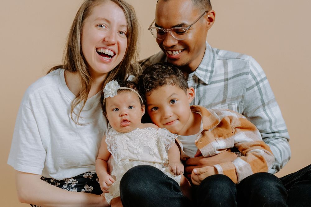 Biracial family of four sitting in a studio laughing at the camera. Delaware Family Photographer