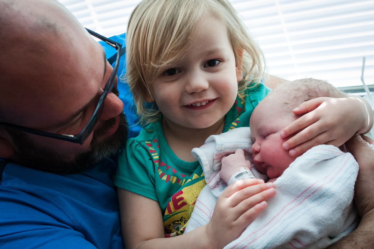 dad holding his little girl as she holds her new little sister for the first time just after she was born.