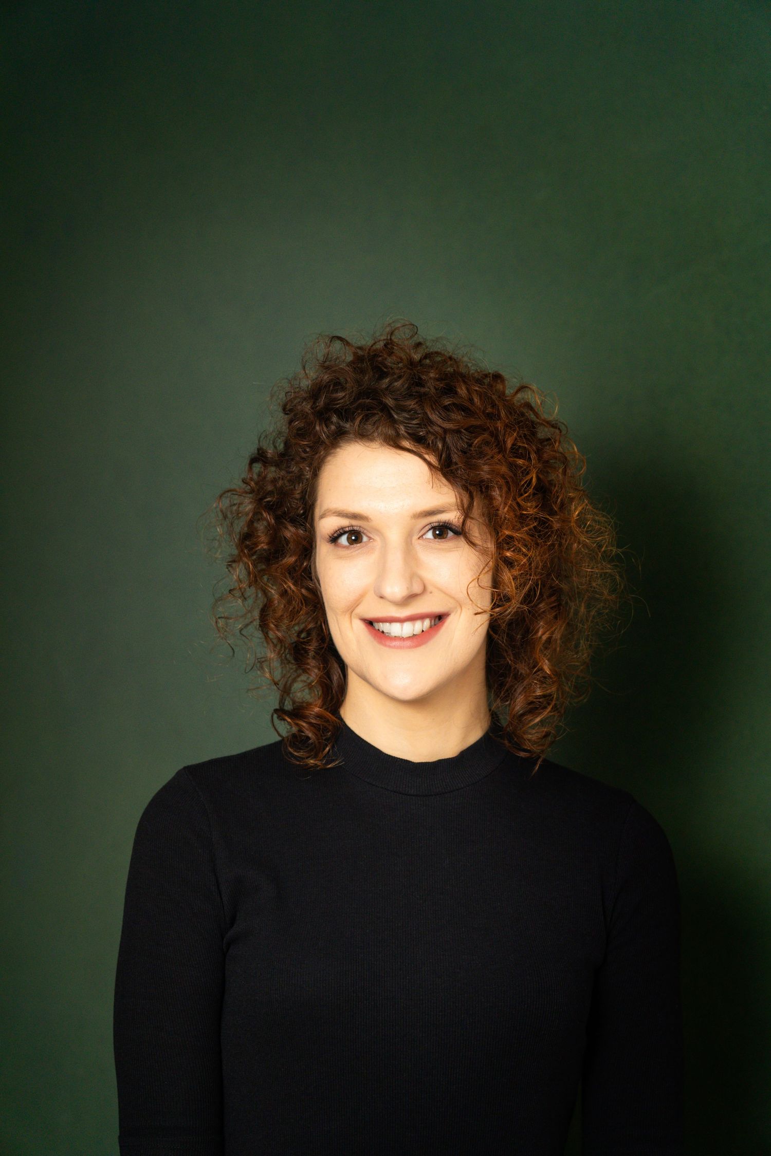 Professional headshot featuring natural curls against a deep green background.