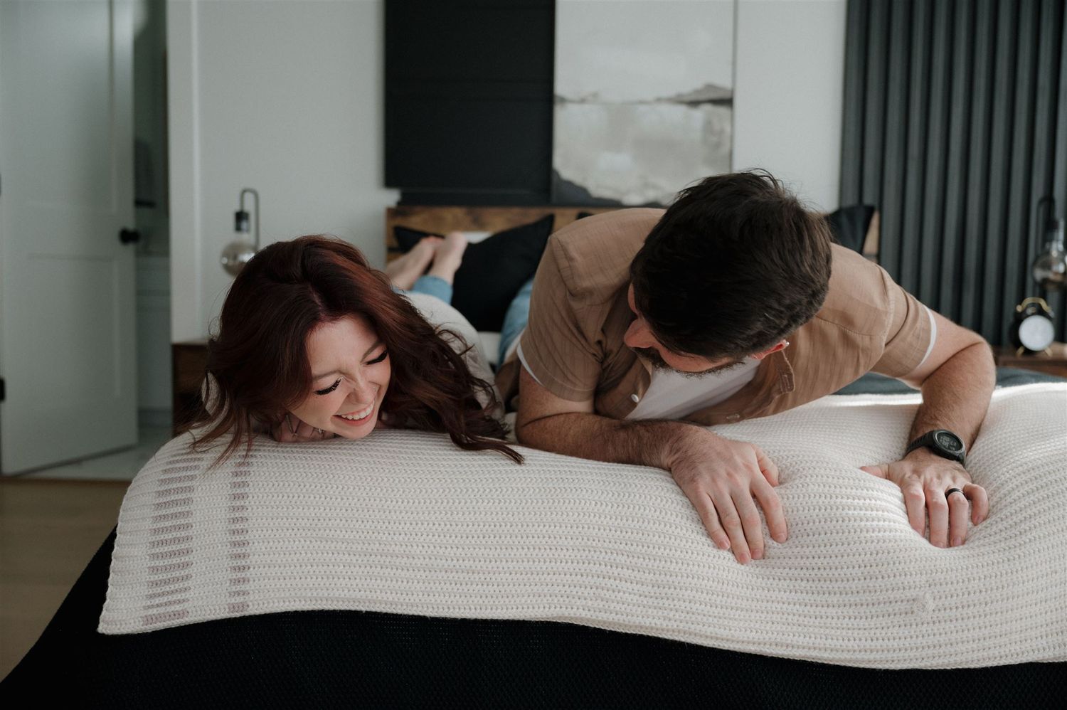 Two people sharing a playful moment on white bedding in a modern bedroom.