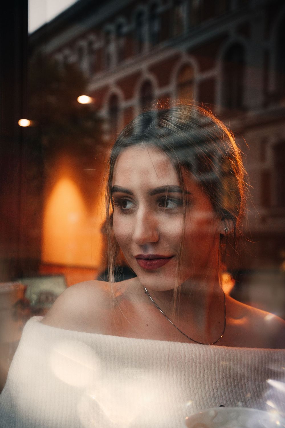 Hangulatos női portré ablakon keresztül, városi háttérrel – lifestyle vagy fine art fotó, mélyebb érzelmi hangulattal.