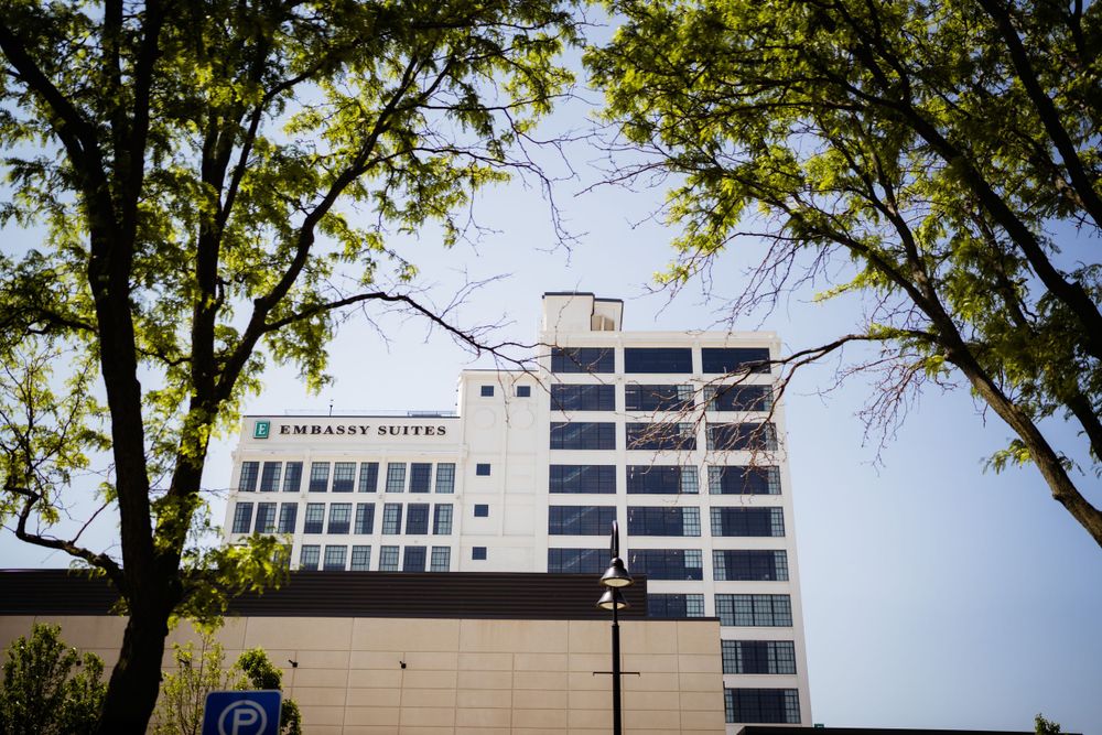 Modern white hotel building framed by green trees against blue sky.