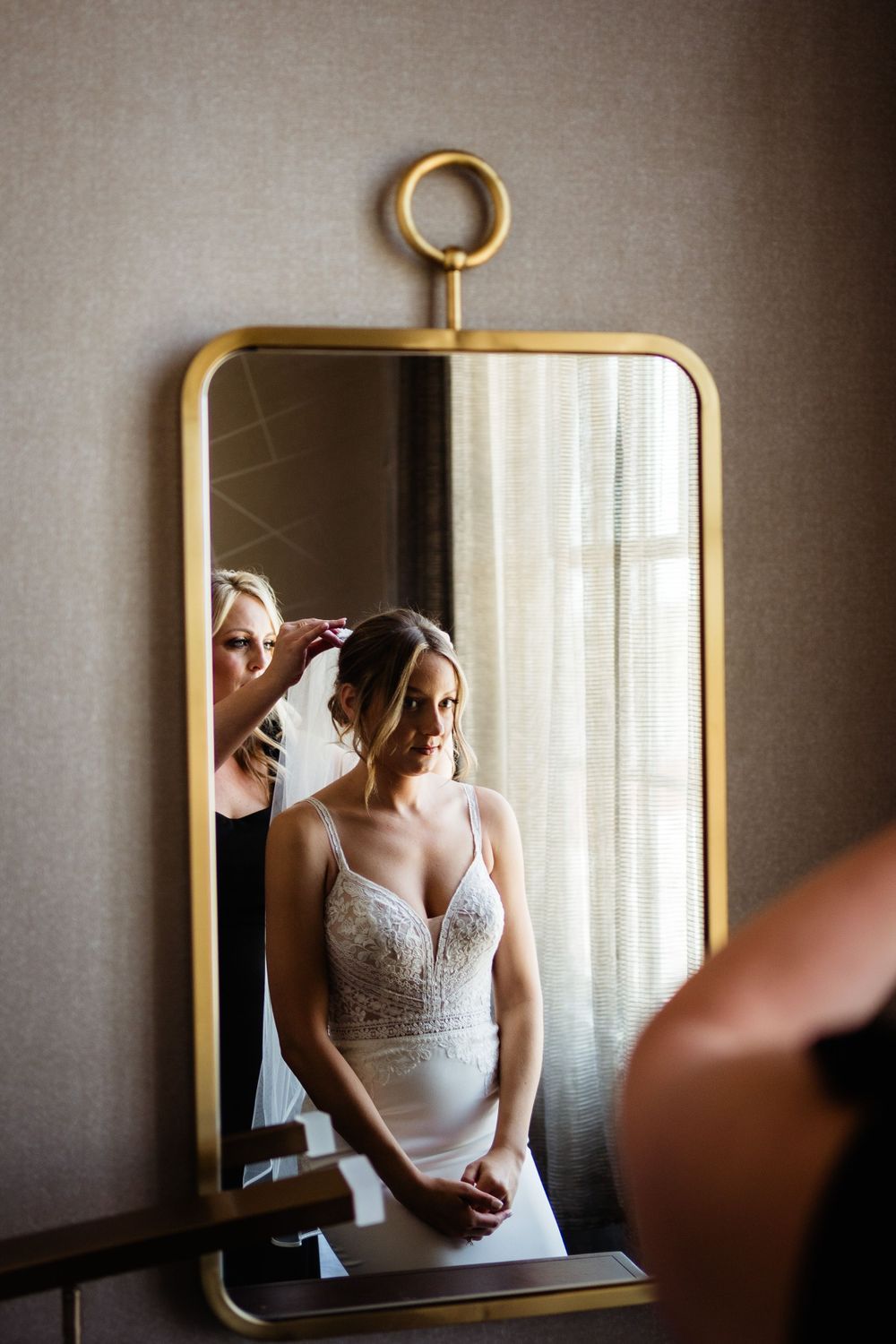Wedding preparations reflected in an elegant gold-framed mirror showing final touches being made to bridal attire.