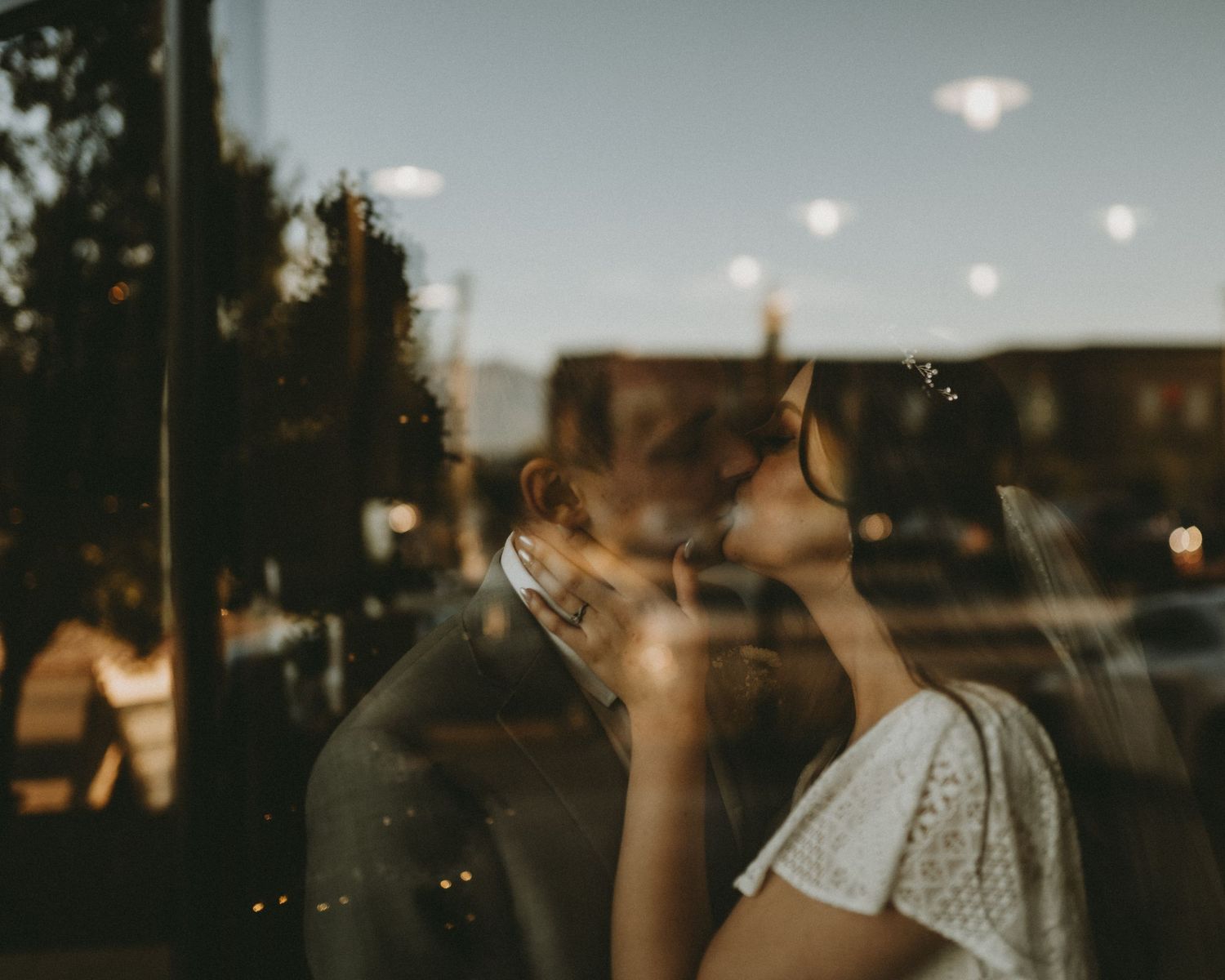 Intimate reflection of couple through window glass at twilight with city lights.