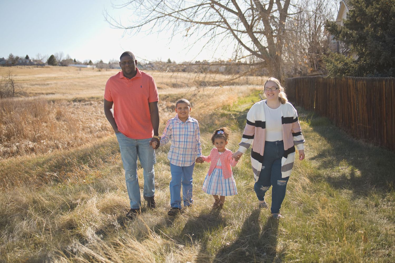 biracial family of four holding hands walking portrait