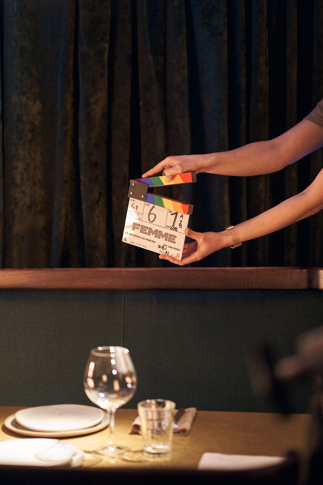 A movie slate board being held over a set table with wine glasses.