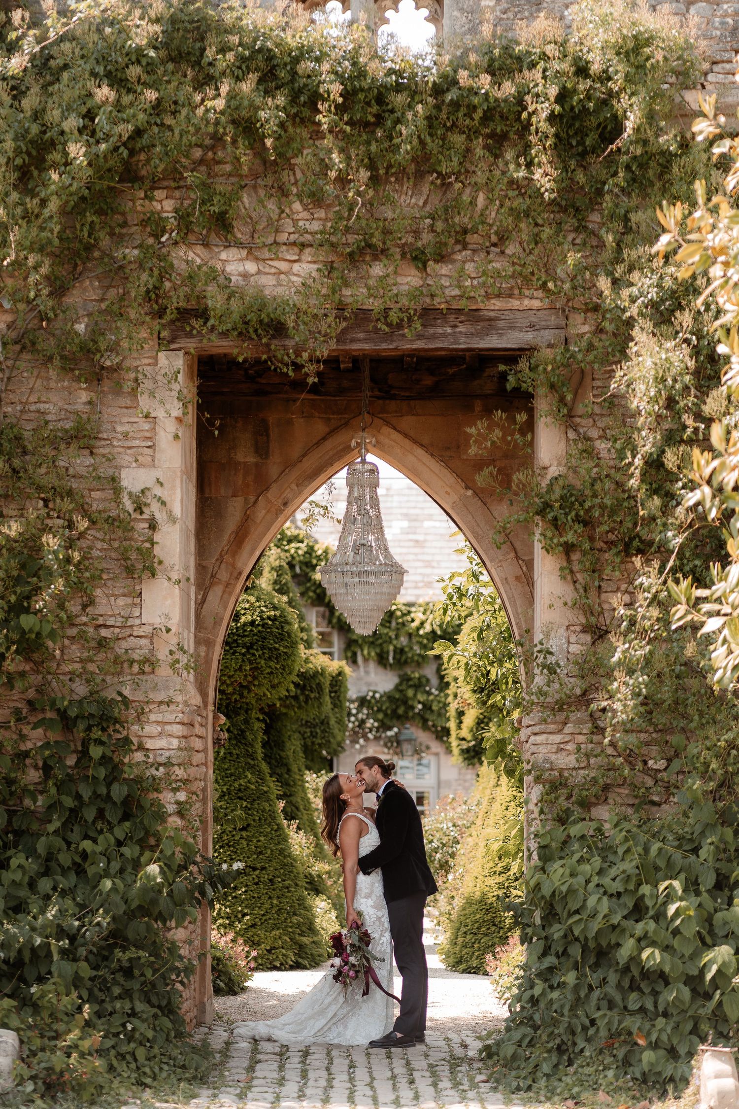 A couple laugh and kiss together under the castle arch chandelier at Euridge Manor, a luxury Cotswolds wedding venue