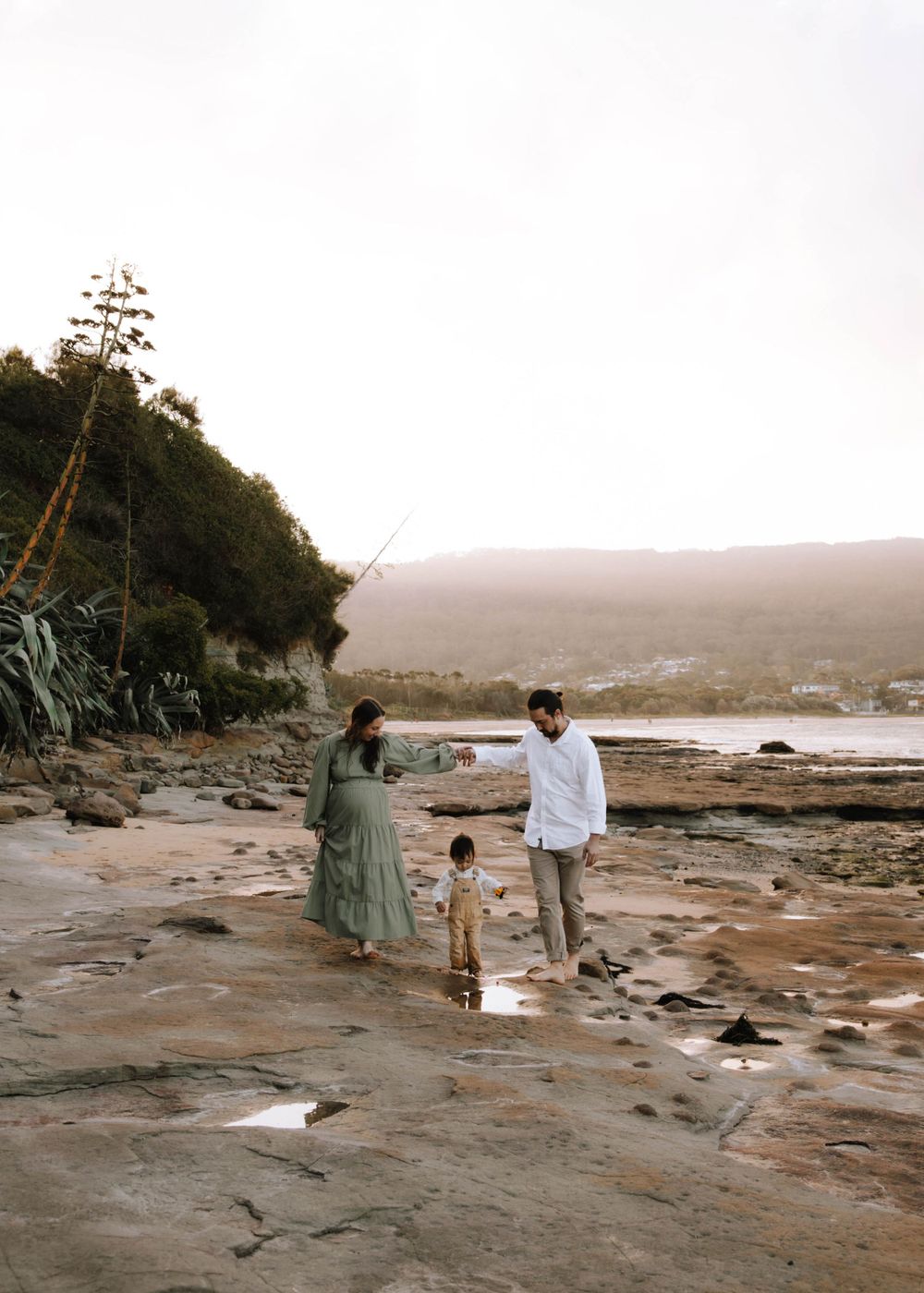 Mum, dad and their toddler sharing a peaceful moment on a beach in the sunshine. Family and maternity outdoor photoshoots in Wollongong.