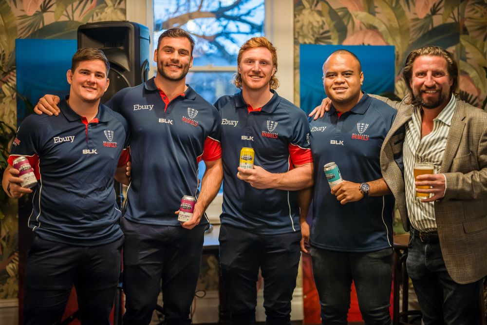 Five men in matching rugby jerseys posing together at an indoor sports promotional event.