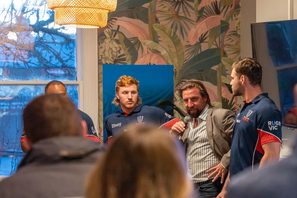 Rugby players and guests engaged in discussion at an intimate indoor sports meet-and-greet event.