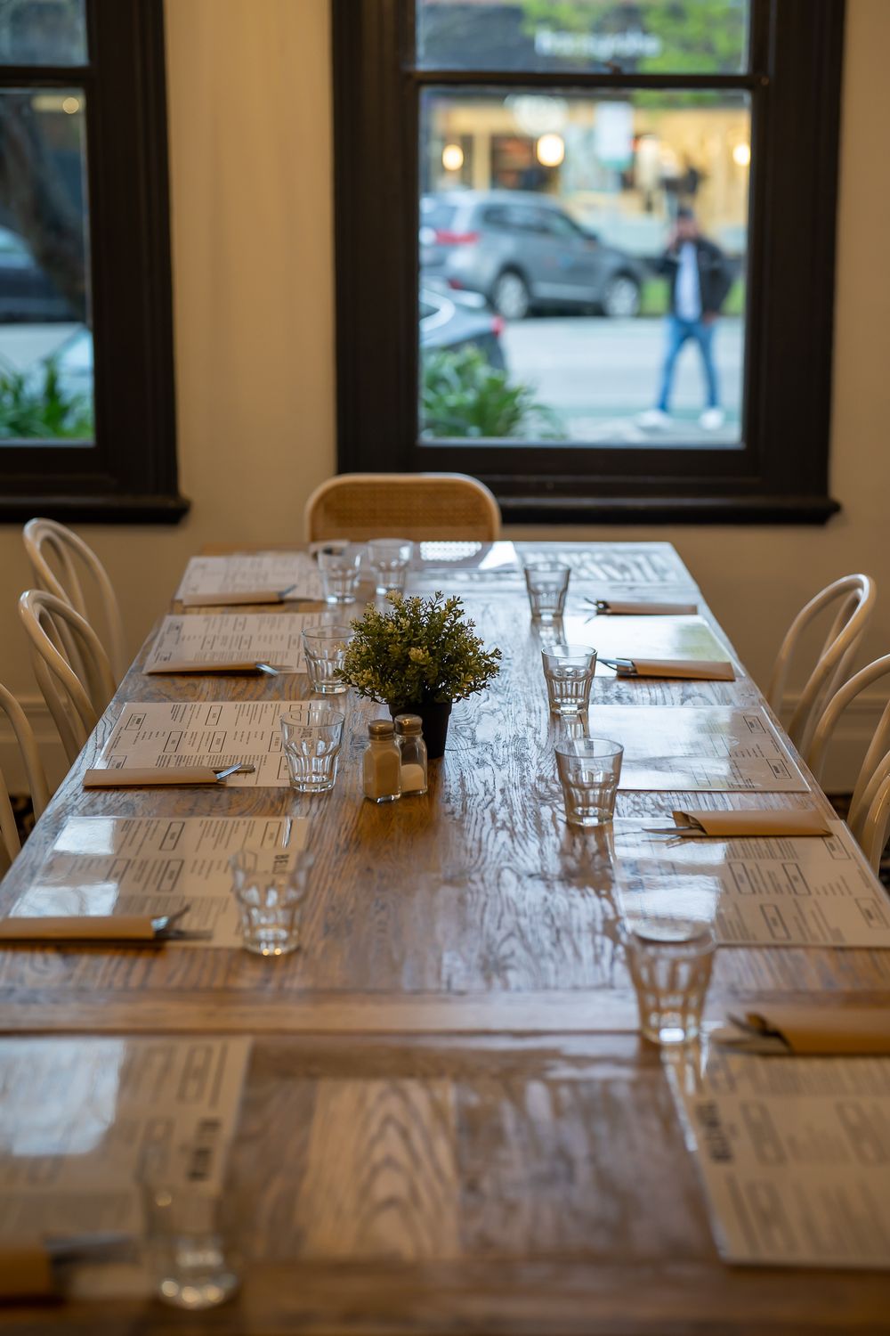 Neatly set wooden dining table with menus, glasses and a small plant centerpiece.