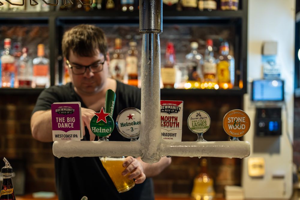 Male bartender pouring a draft Heineken beer at a pub bar.