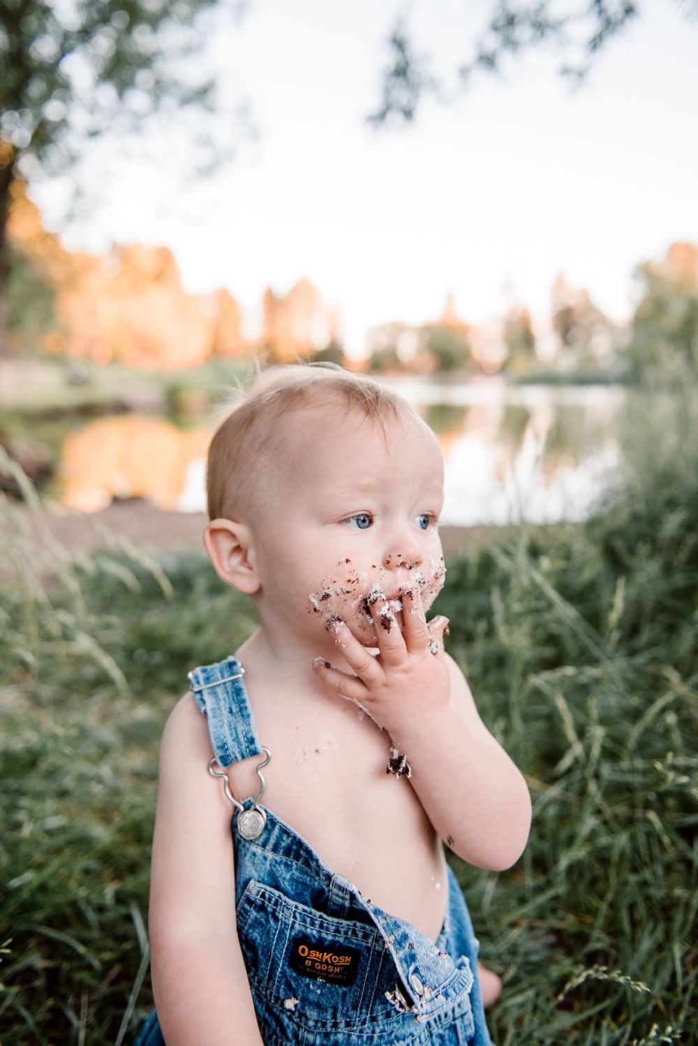 Toddler in denim overalls with cake-covered face during outdoor photoshoot.