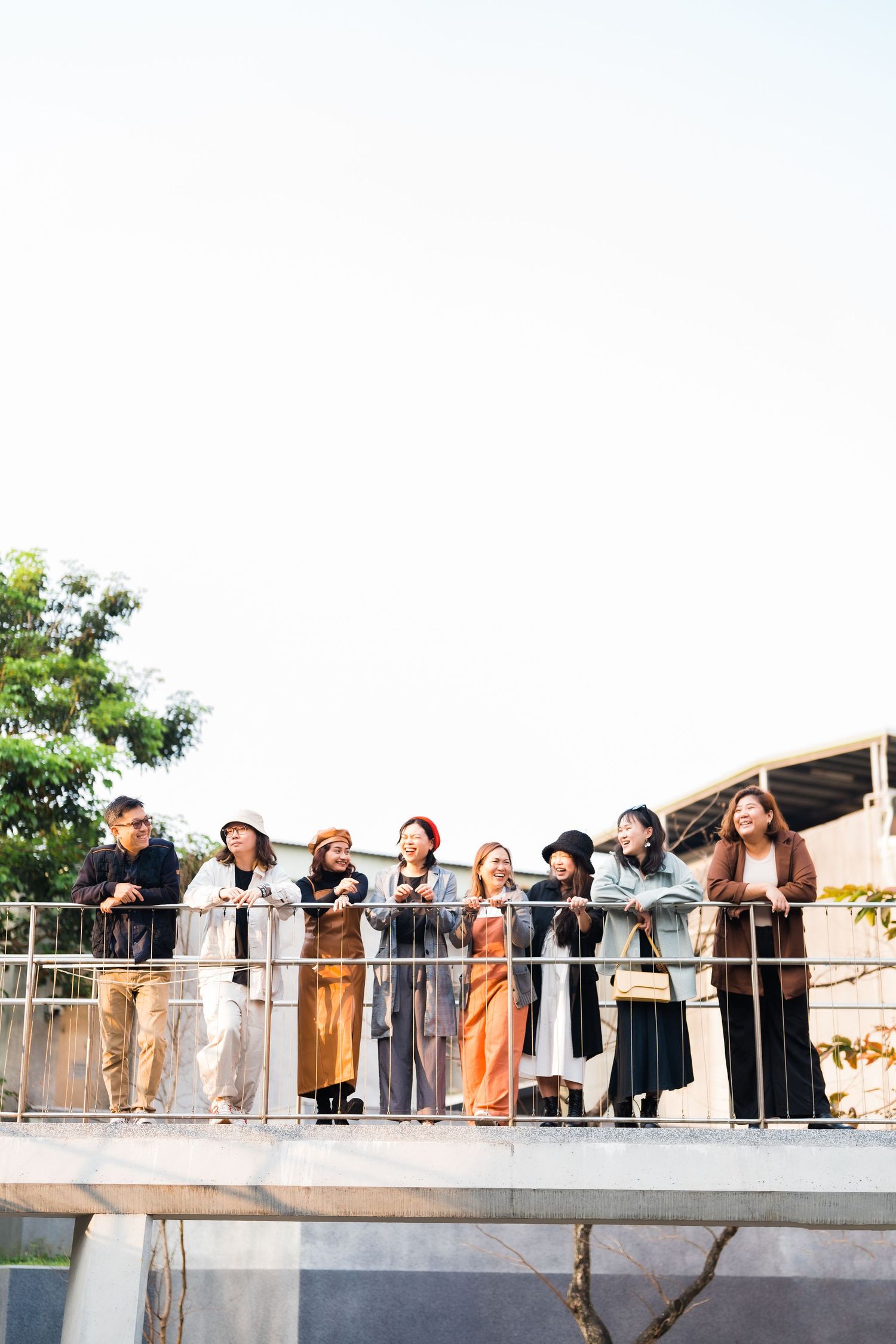 A group of friends standing together on a balcony railing against a white sky.