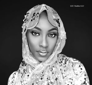 Artistic black and white portrait featuring delicate lace headpiece and striking makeup against dark background.