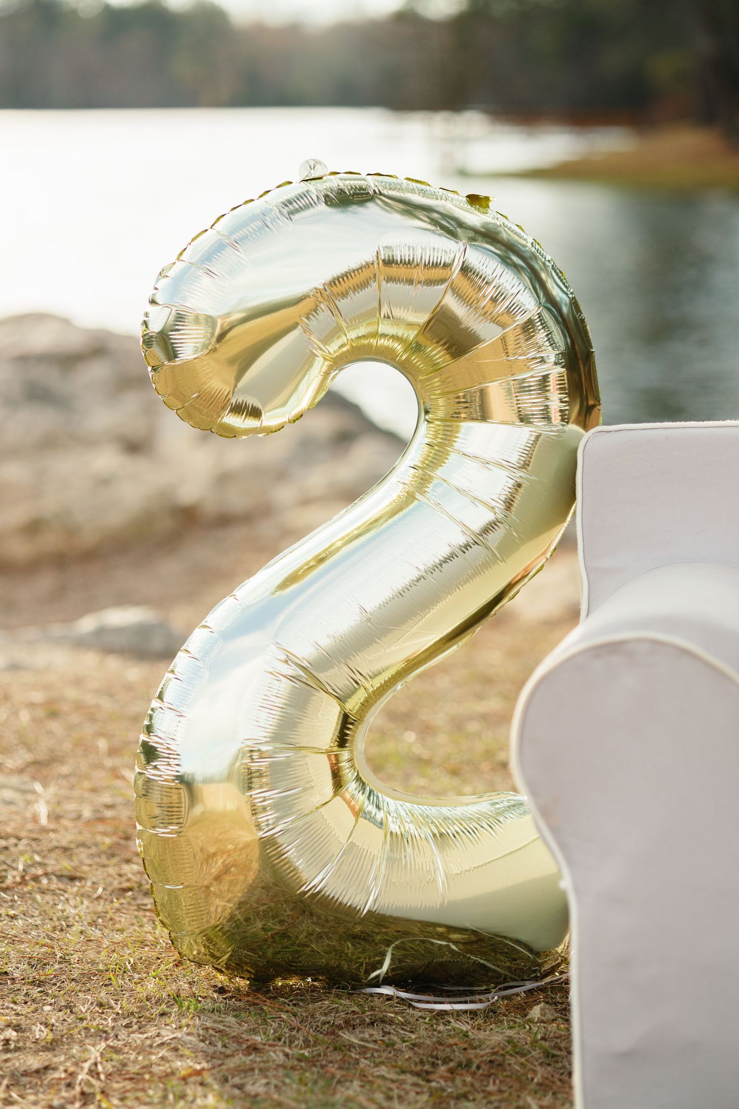 Large gold metallic number 2 balloon stands against an outdoor backdrop with water.