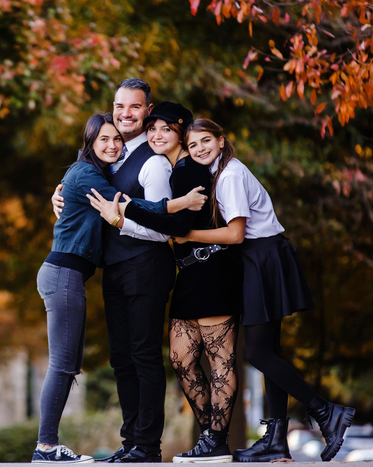 Group of friends hugging and smiling together during autumn with fall foliage in background.