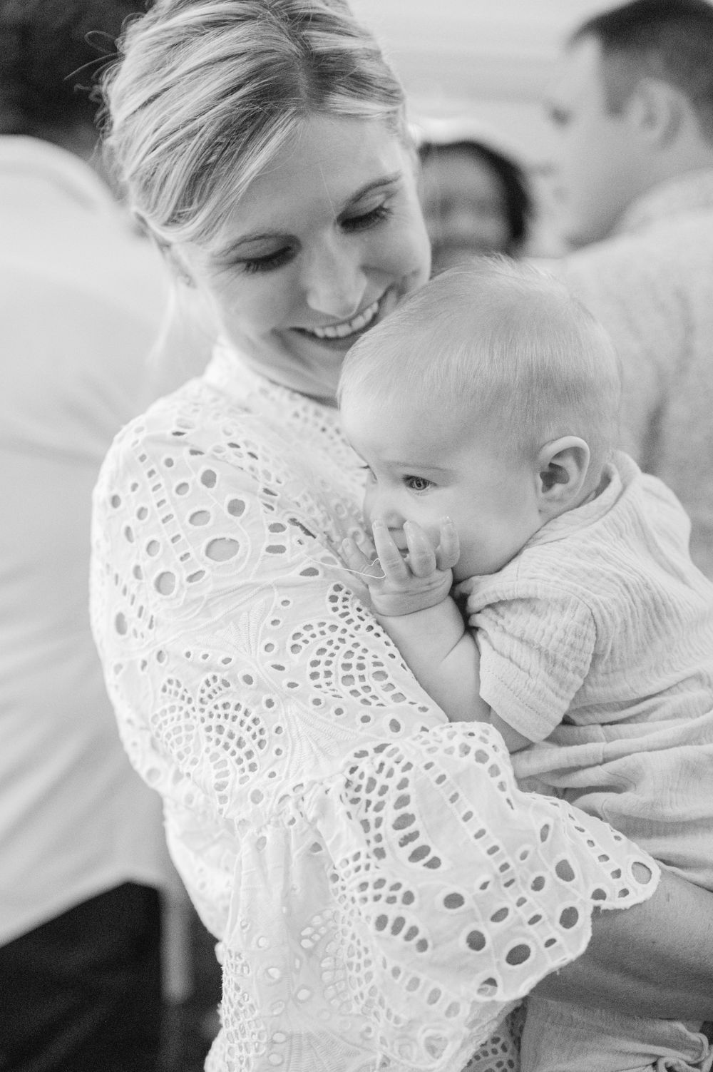 An intimate black and white portrait of maternal affection with a baby in a lace dress.