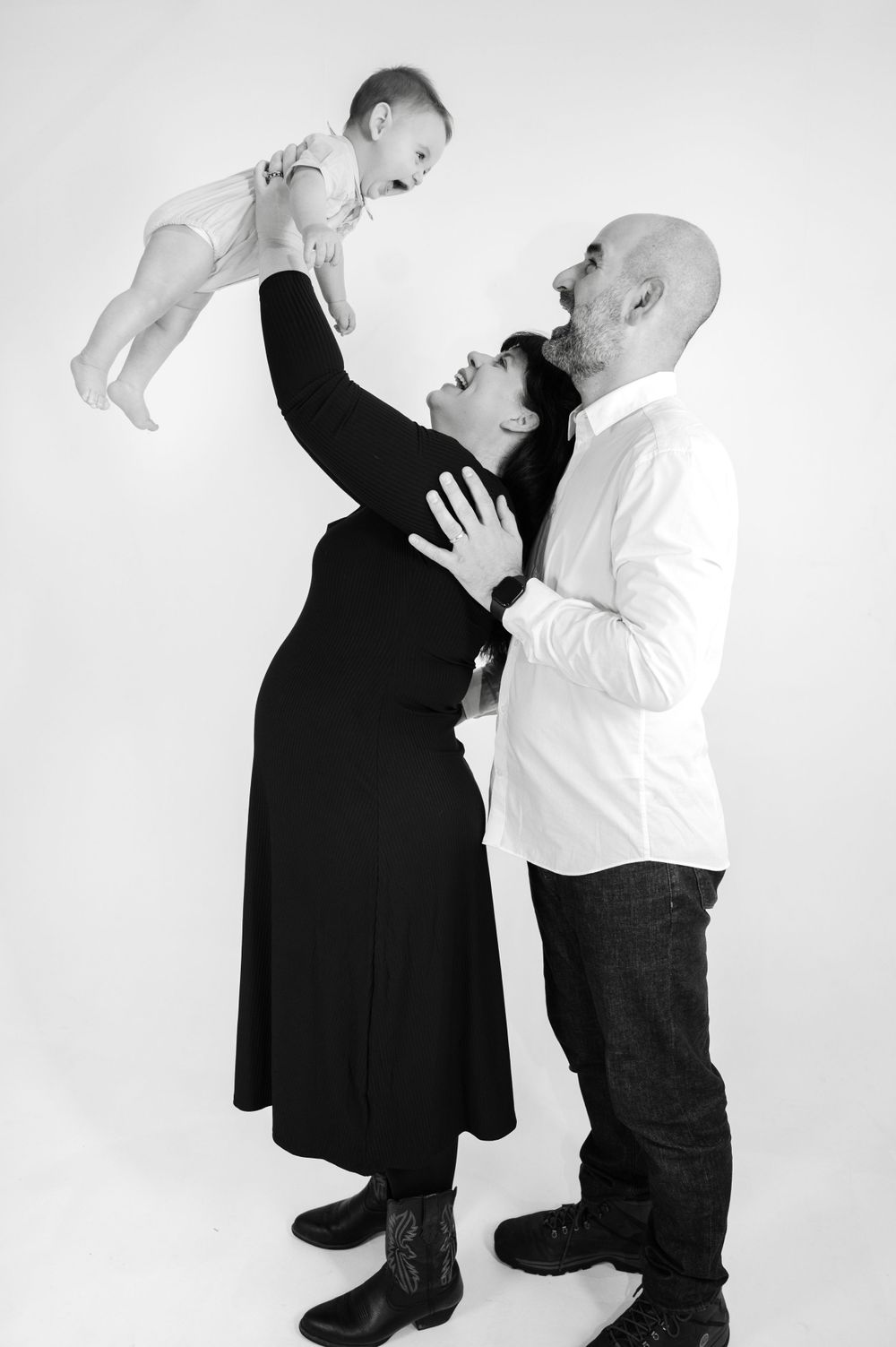 A black and white portrait of a family lifting their baby up in playful moment.