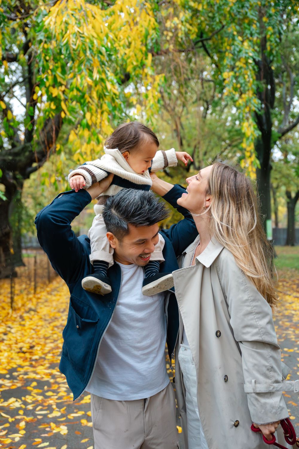 A family enjoying autumn day in park with yellow leaves and trees in background.