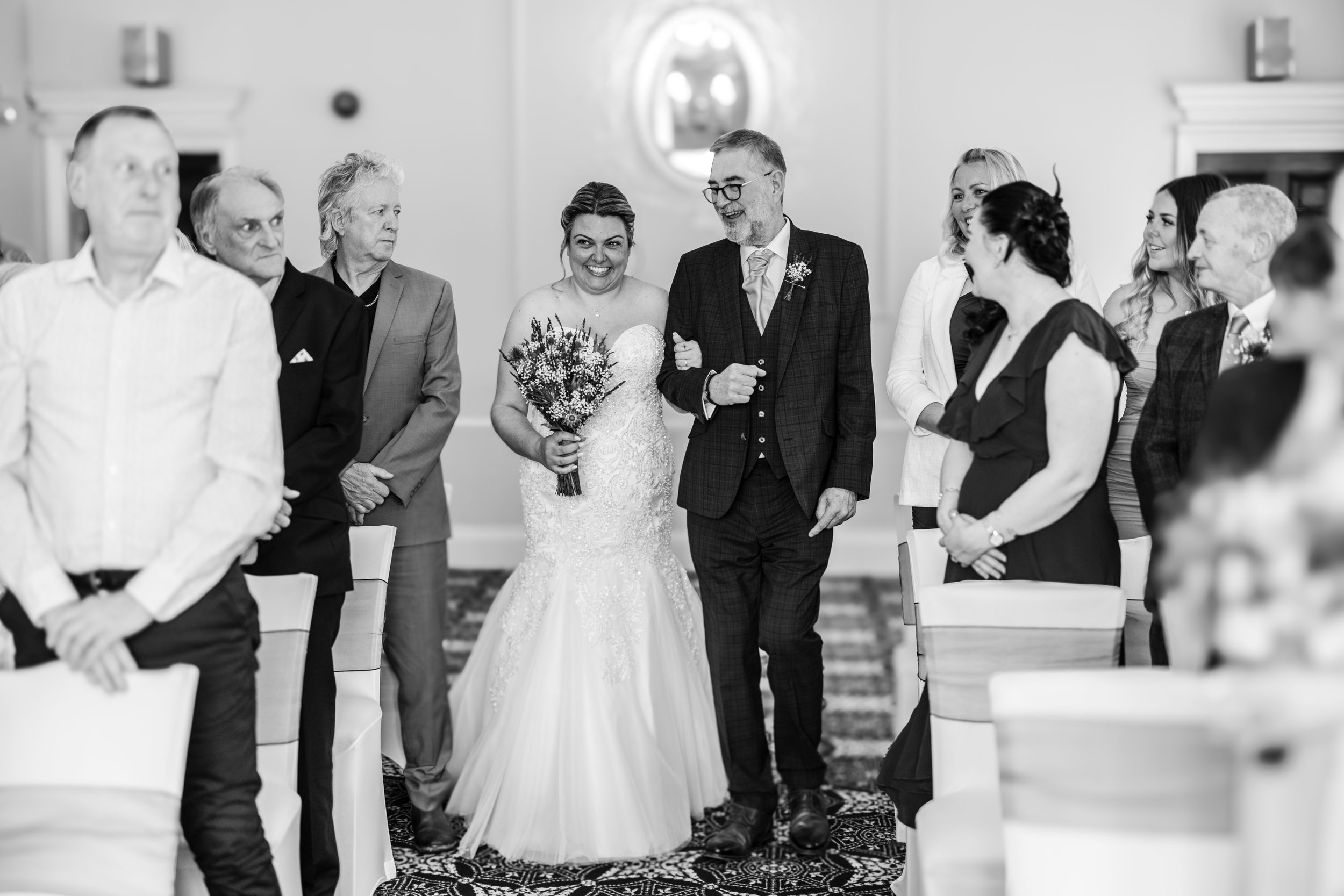 Black and white candid moment of wedding celebration with guests laughing.