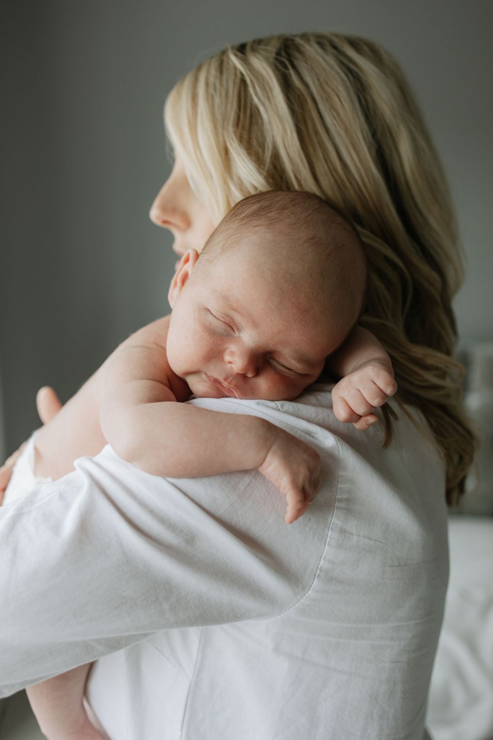 Sleeping infant rests peacefully on shoulder in gentle lighting.