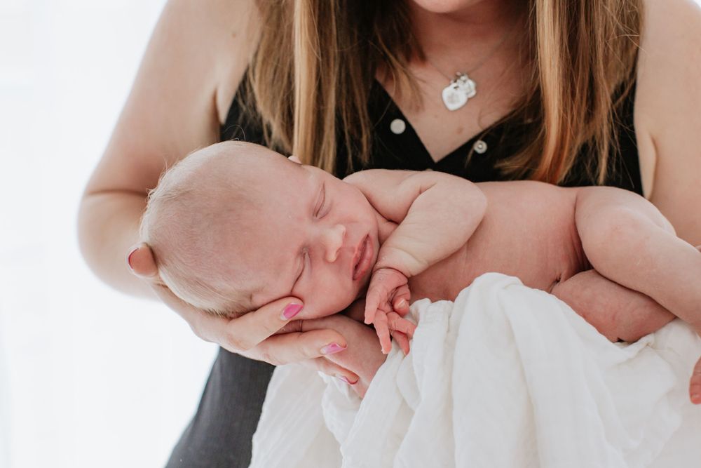 Sleeping newborn baby cradled in caregiver's arms with white background.