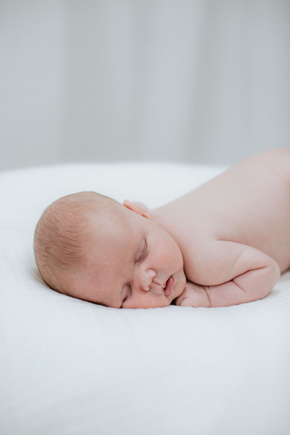 Peaceful newborn baby sleeping on white sheets in soft lighting.