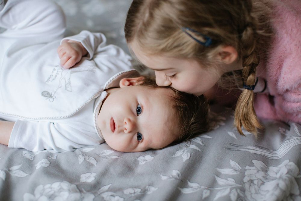 Tender moment between siblings as they cuddle on bed together.