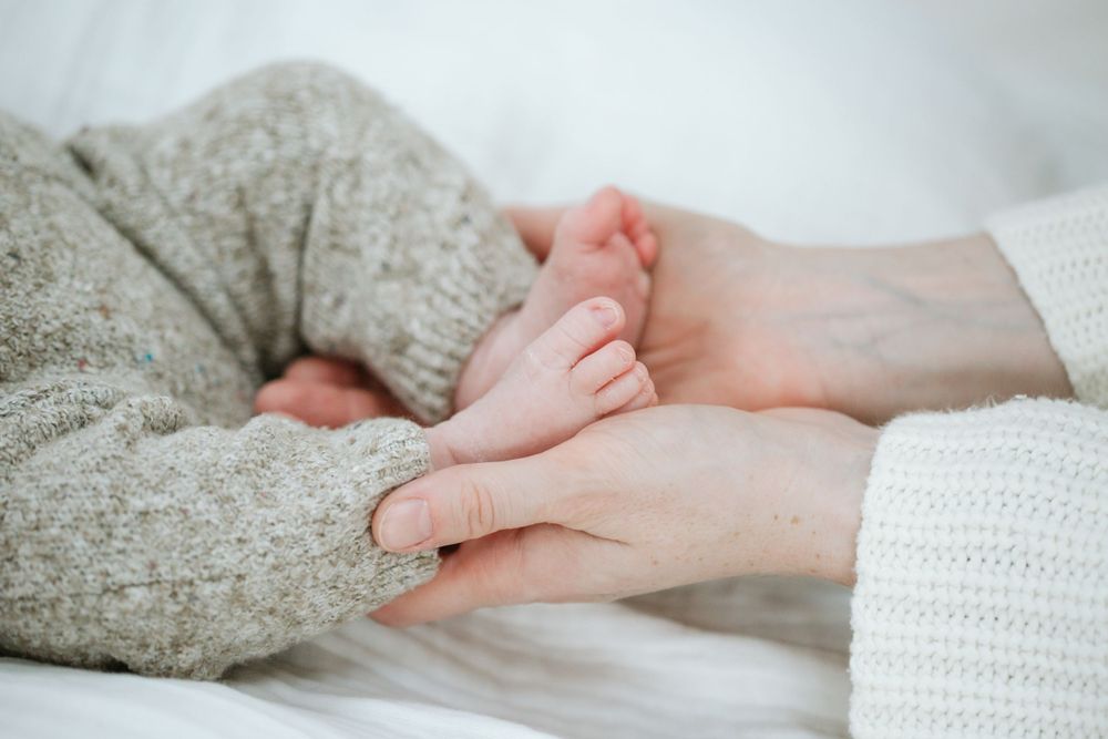 Gentle hands cradle tiny baby feet wrapped in soft gray knit fabric.