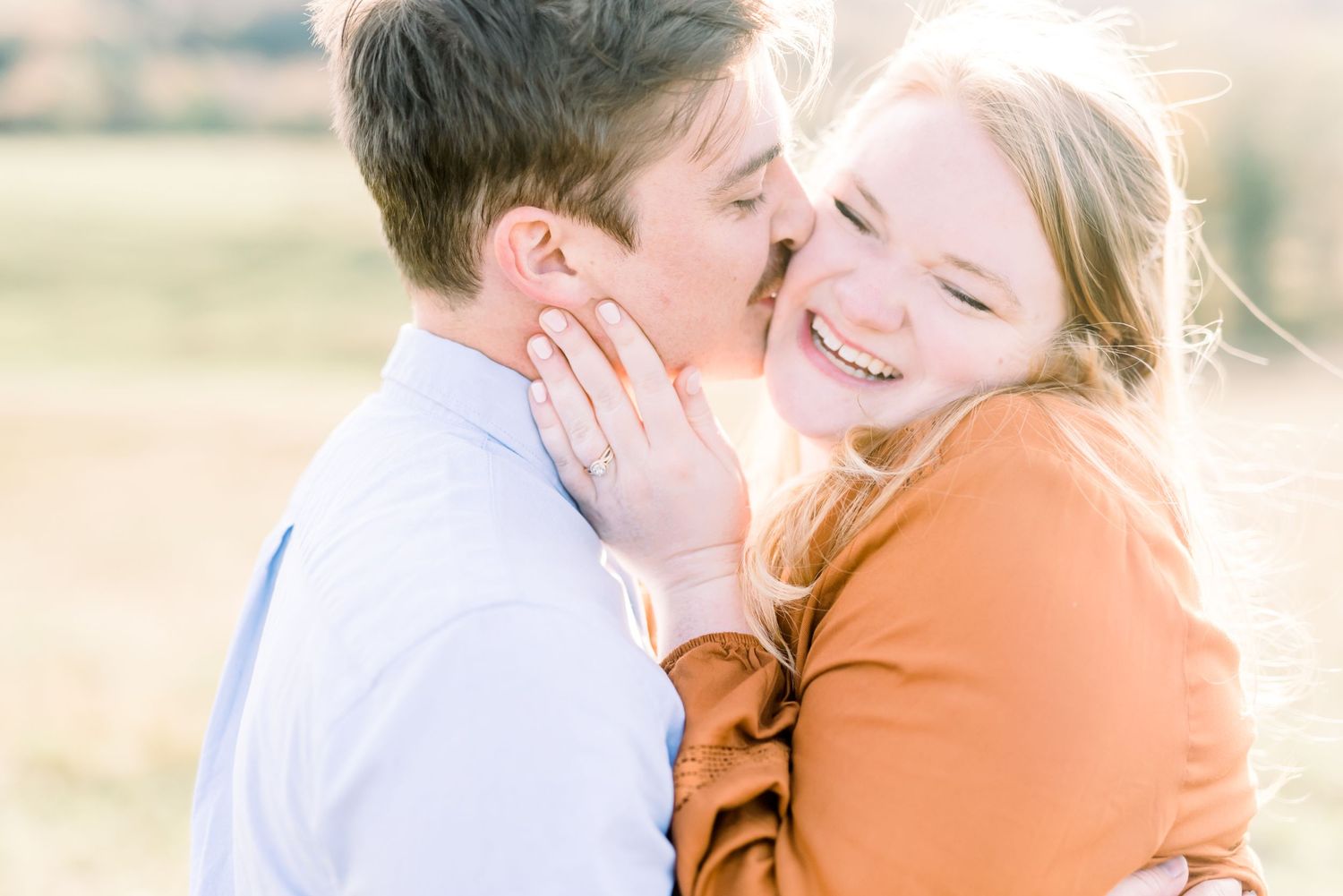 Happy couple snuggling close to each other in warm golden sunlight during outdoor photoshoot.