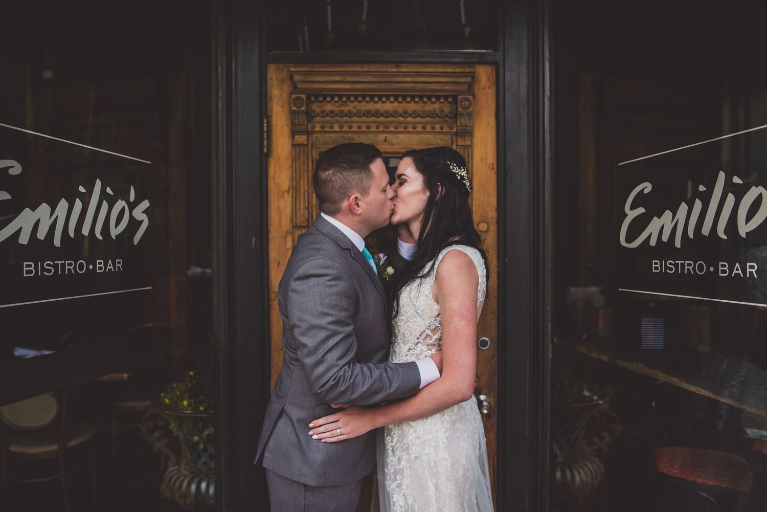 Wedding couple sharing a romantic kiss in front of Emilio's Bistro Bar entrance doors.