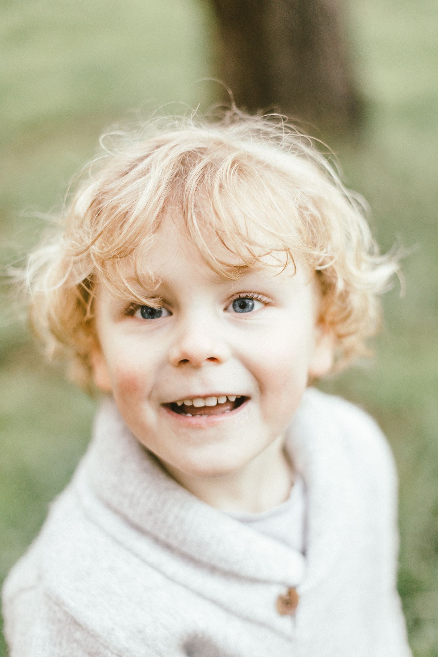 Close-up portrait of a smiling toddler with curly blonde hair wearing a light grey sweater.