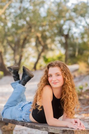 senior laying on park bench in park during fun candid senior portrait photoshoot in Panama City Beach Florida