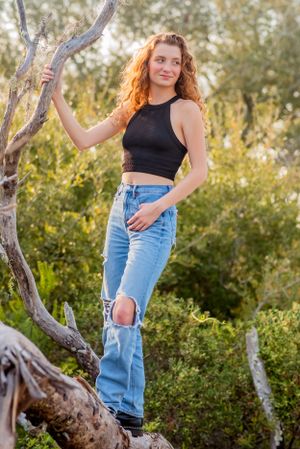 senior climbing a tree in park during fun candid senior portrait photoshoot in Panama City Beach Florida