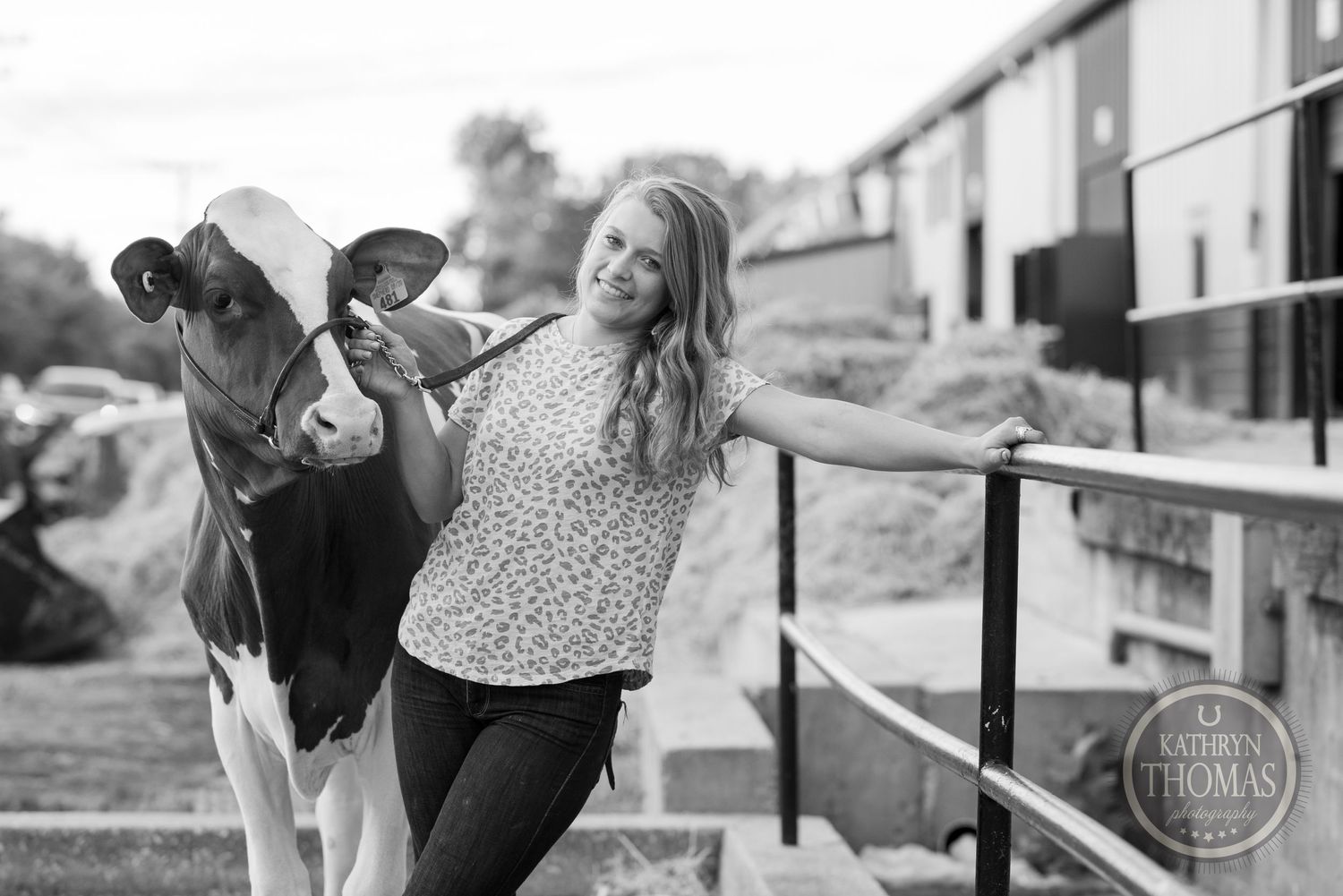 A monochrome image of a Holstein cow and person leaning against metal fencing at a farm event.