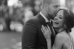 A black and white wedding photo capturing a joyful intimate moment between newlyweds.