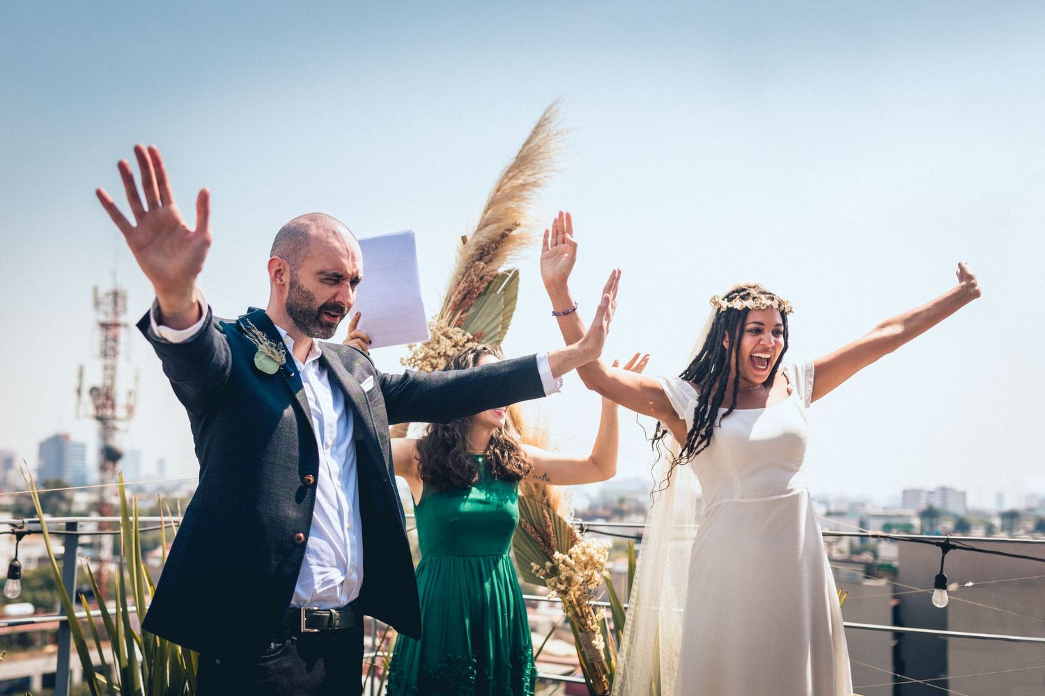 Wedding celebration on a rooftop terrace with guests raising their arms in joyful celebration.