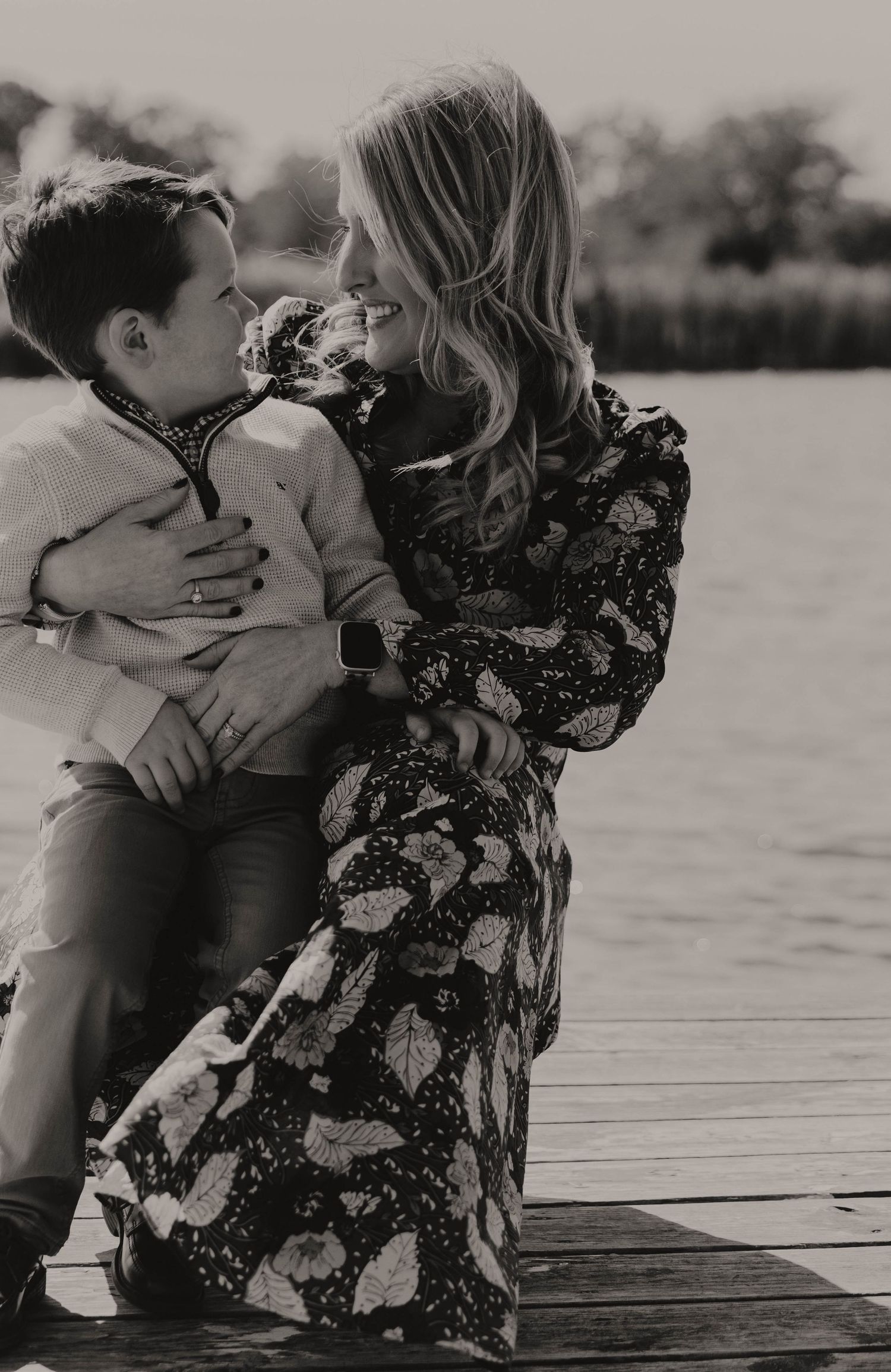 Mother and child sharing tender moments on wooden dock by the water.