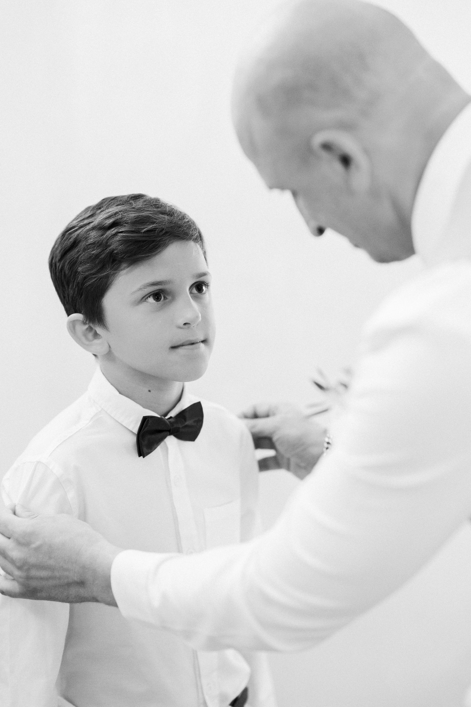 A tender moment of preparation between two people in formal white attire.