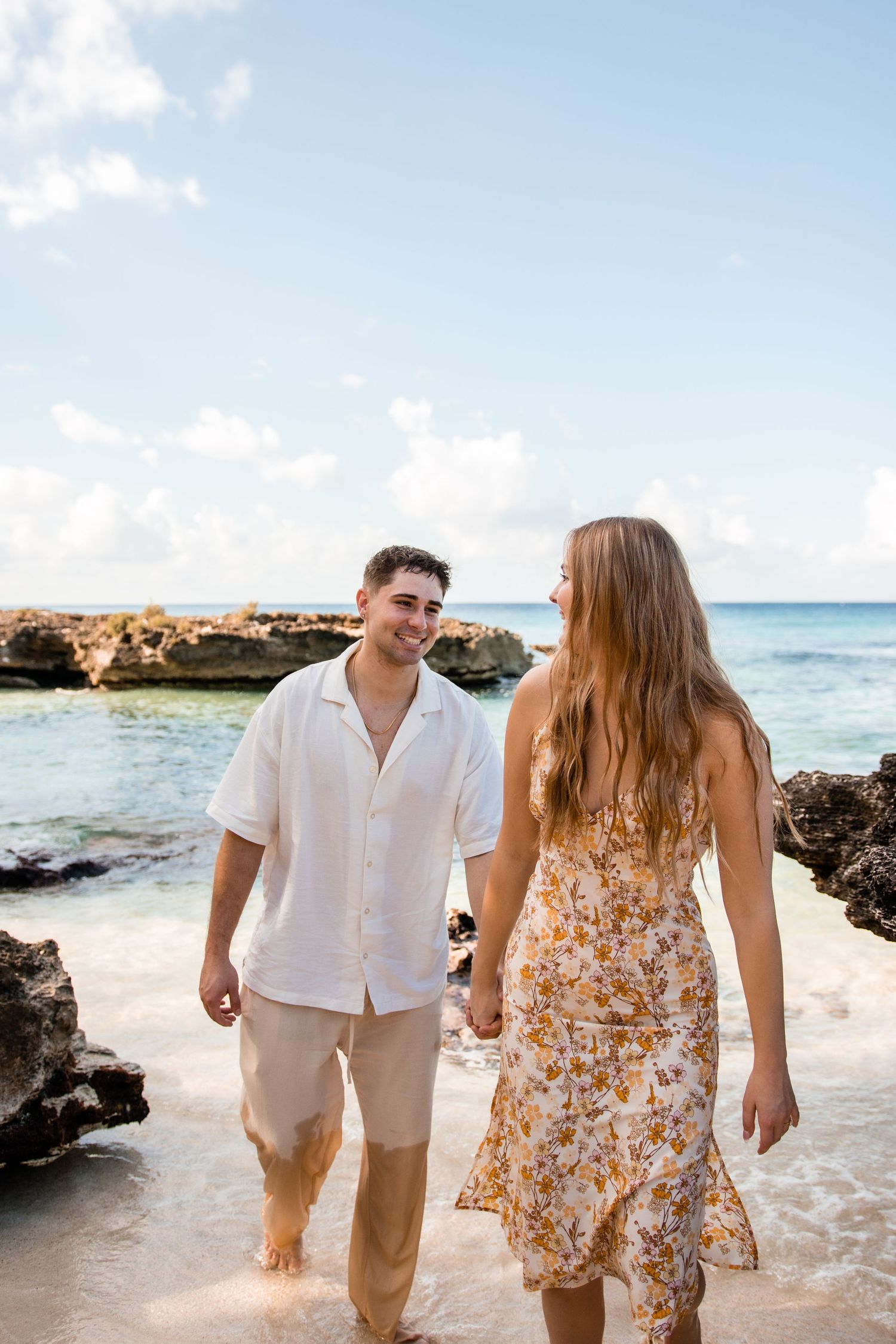 Couple strolls along pristine beach with turquoise waters and volcanic rocks.